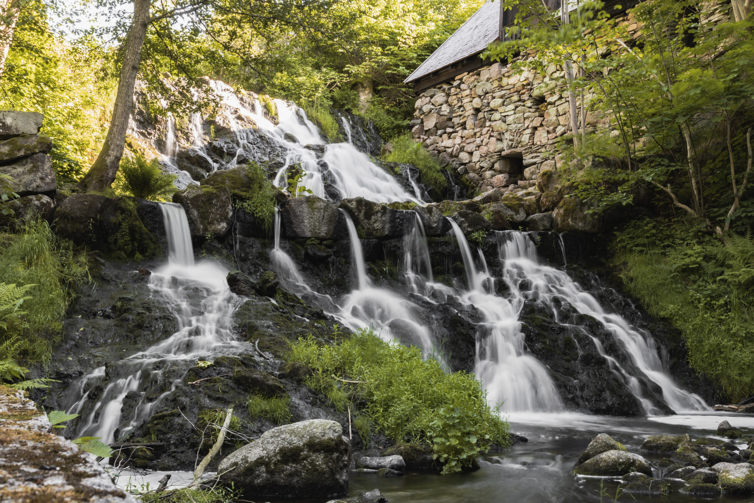 Vattenfall vid stenbyggnad i skogsmiljö